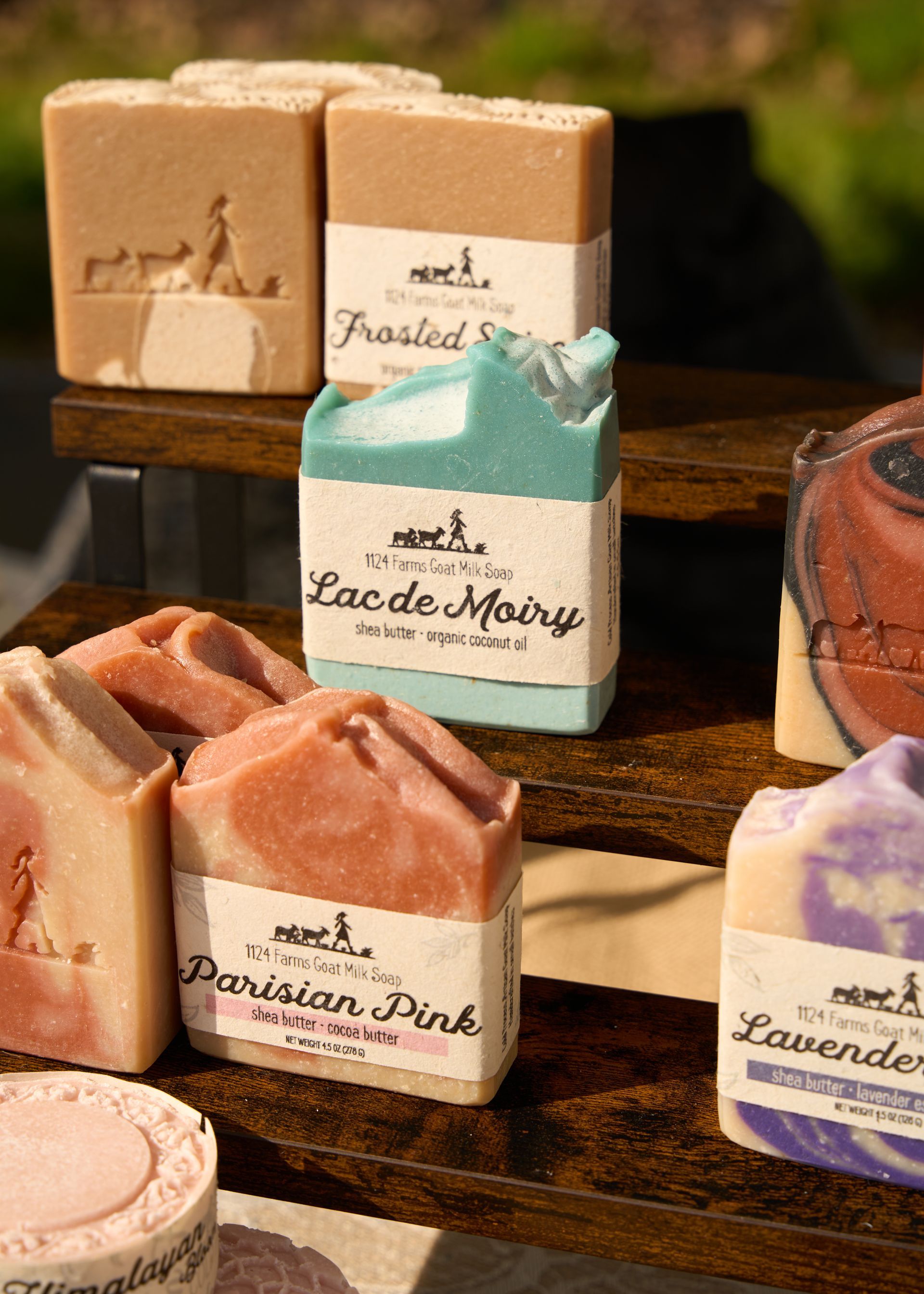 Assorted handmade soaps in pastel colors neatly arranged on wooden shelves and display tables at the Loomis Community Farmers Market