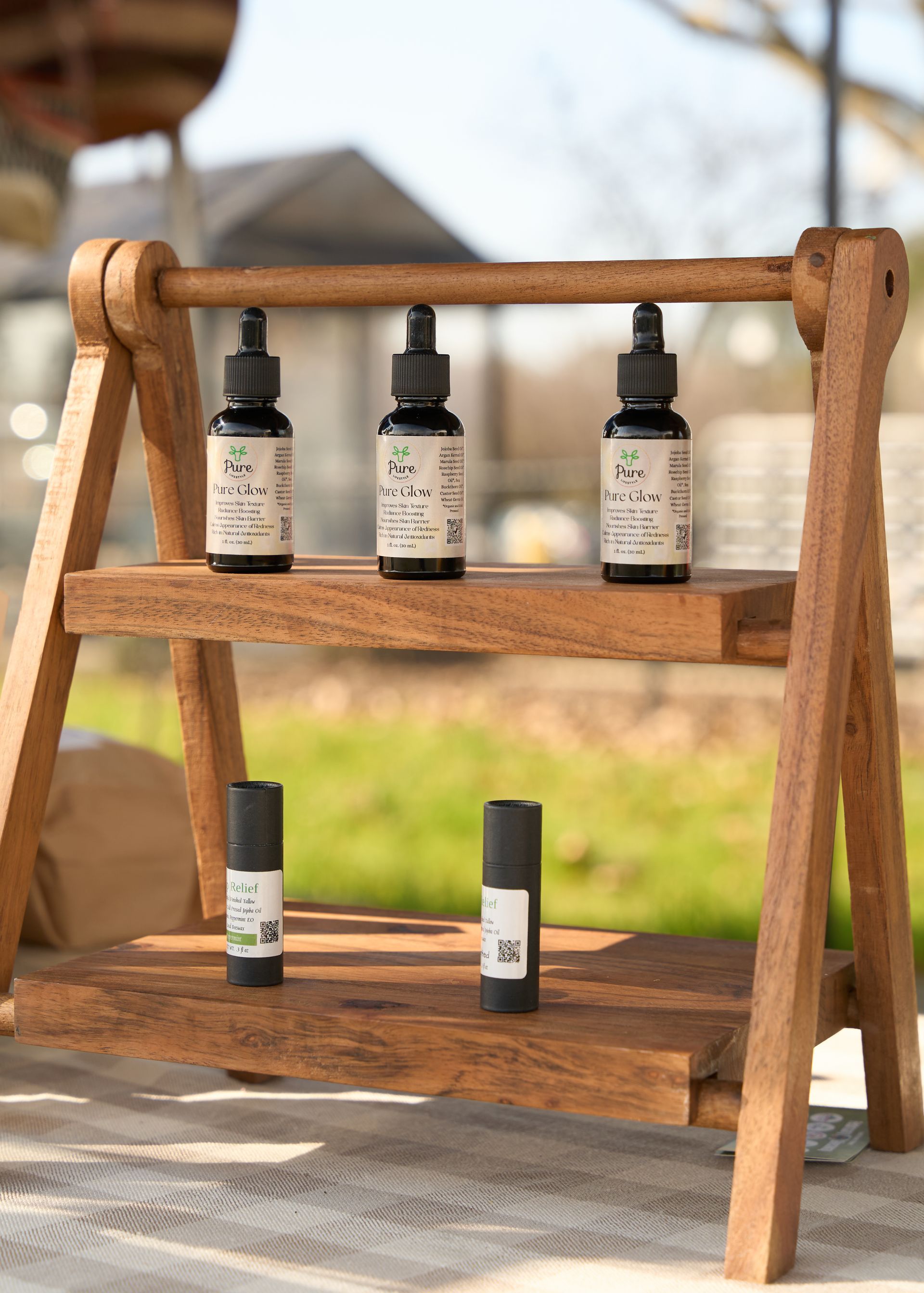 Three natural cosmetic bottles displayed on a wooden stand in warm sunlight at the Loomis Community Farmers Market