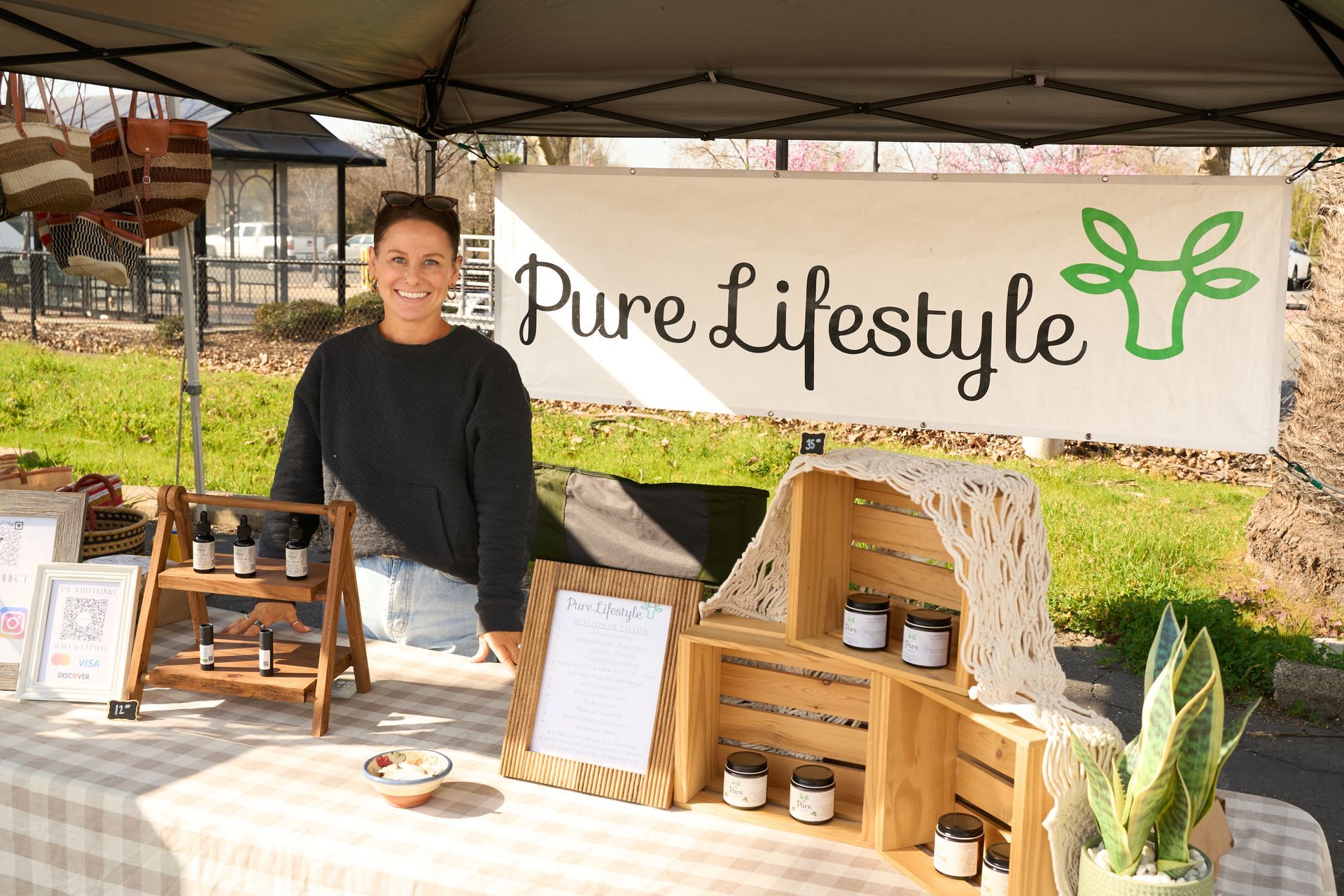 Vendor standing behind wooden display shelves with artisan products under a tent with a Purely Lifestyle banner at the Loomis Community Farmers Market