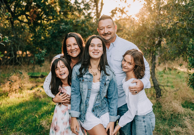 Smiling family of five posing outdoors in a grassy field at sunset