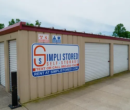 Row of beige self-storage units with white roll-up doors and a Simpli Stored sign on the side.