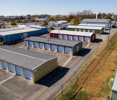 Aerial view of rows of storage units with metal roofs on a paved lot in an industrial area.