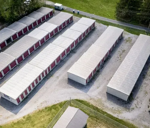 Aerial view of rows of white and red storage units beside a paved road and grassy area