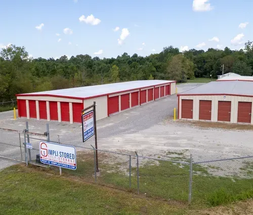 Storage facility with red roll-up doors and a fenced entrance sign on a gravel lot.