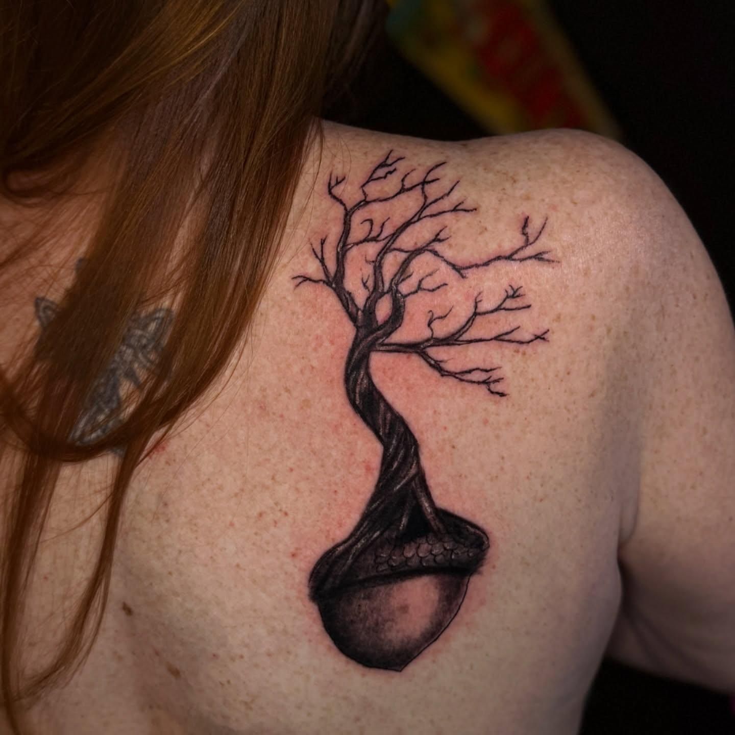 Tattoo of a black tree with bare branches emerging from a large acorn.