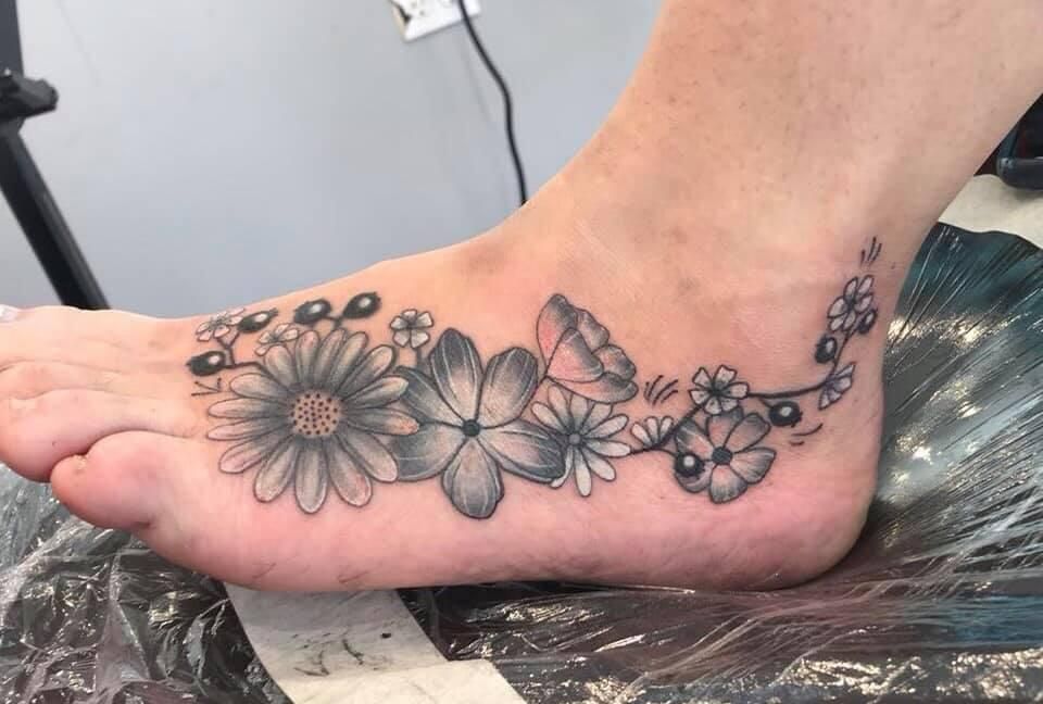 Foot tattoo: grayscale flowers and berries on the top of the foot.