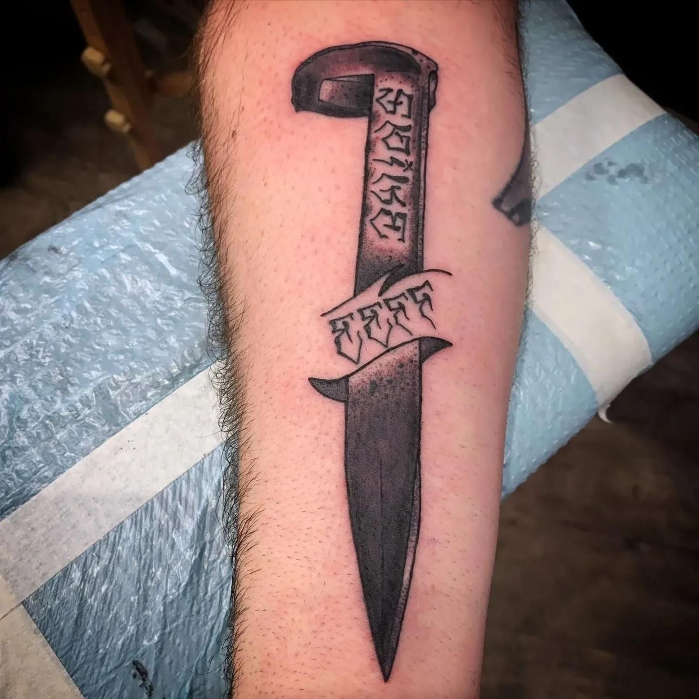 Tattoo of a dagger on a forearm, with text along the blade.