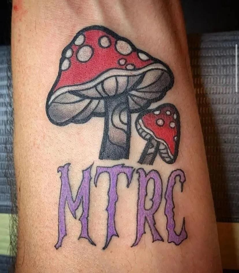 Tattoo of red and white mushrooms above the letters