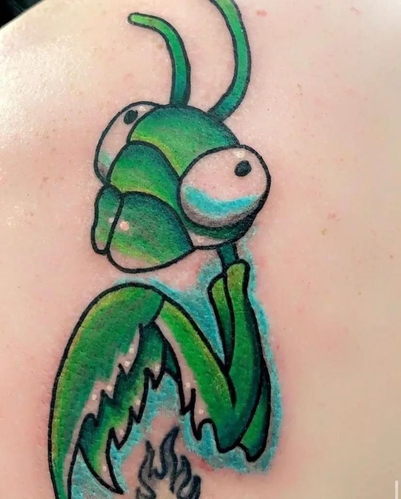 Green praying mantis cartoon tattoo on skin, holding a small fire.