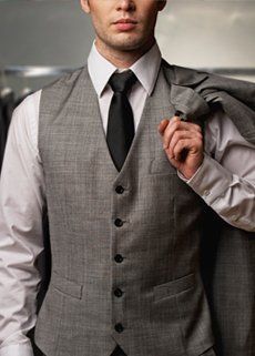 A man in a suit and vest is holding his jacket over his shoulder.