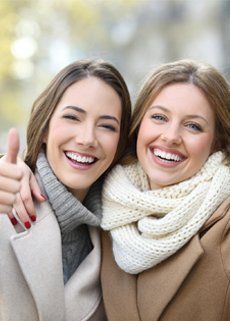 Two women are smiling and giving a thumbs up.