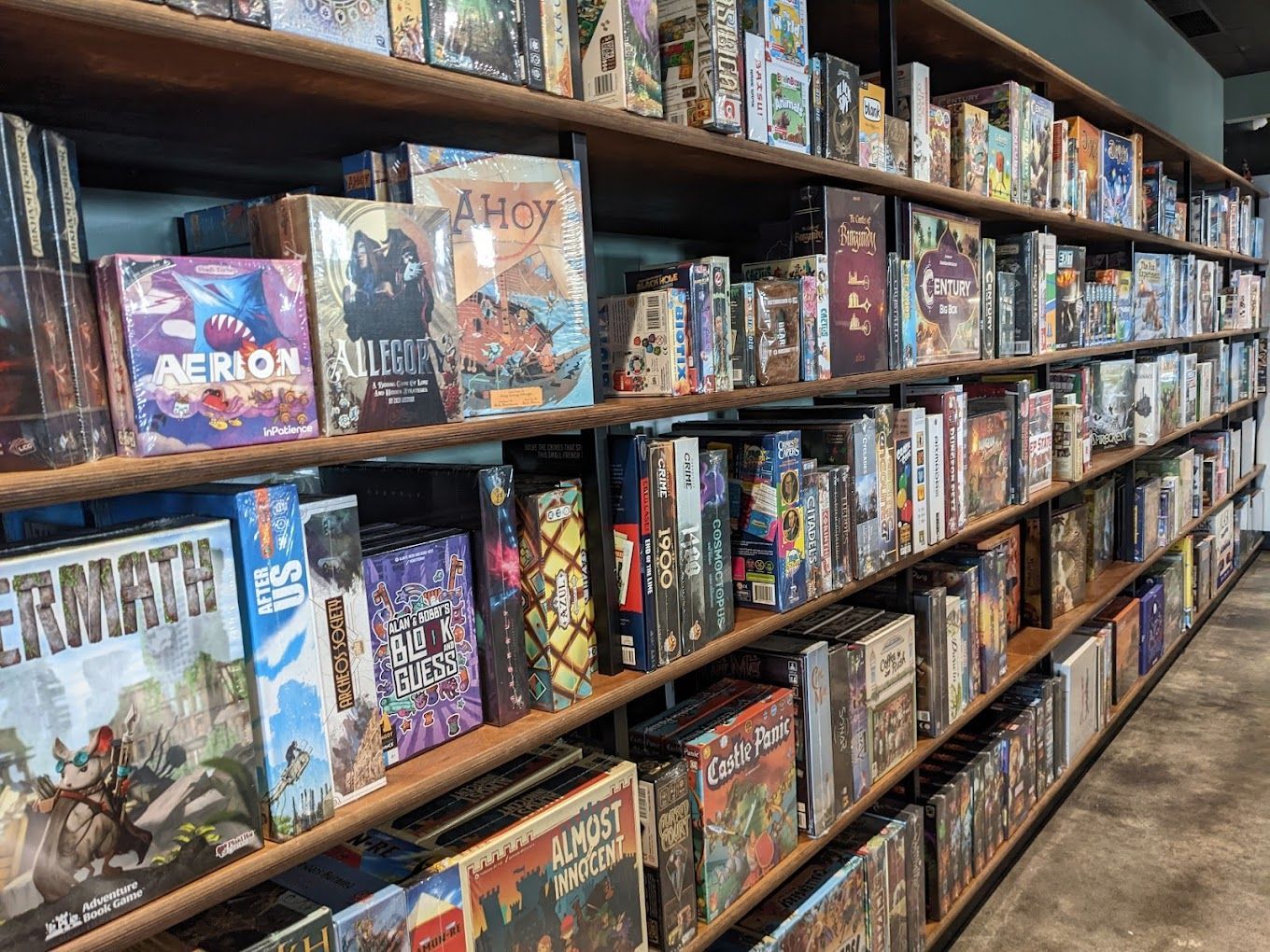 Shelves filled with board games; interior view. Games are diverse with colorful boxes, set against a dark wall.