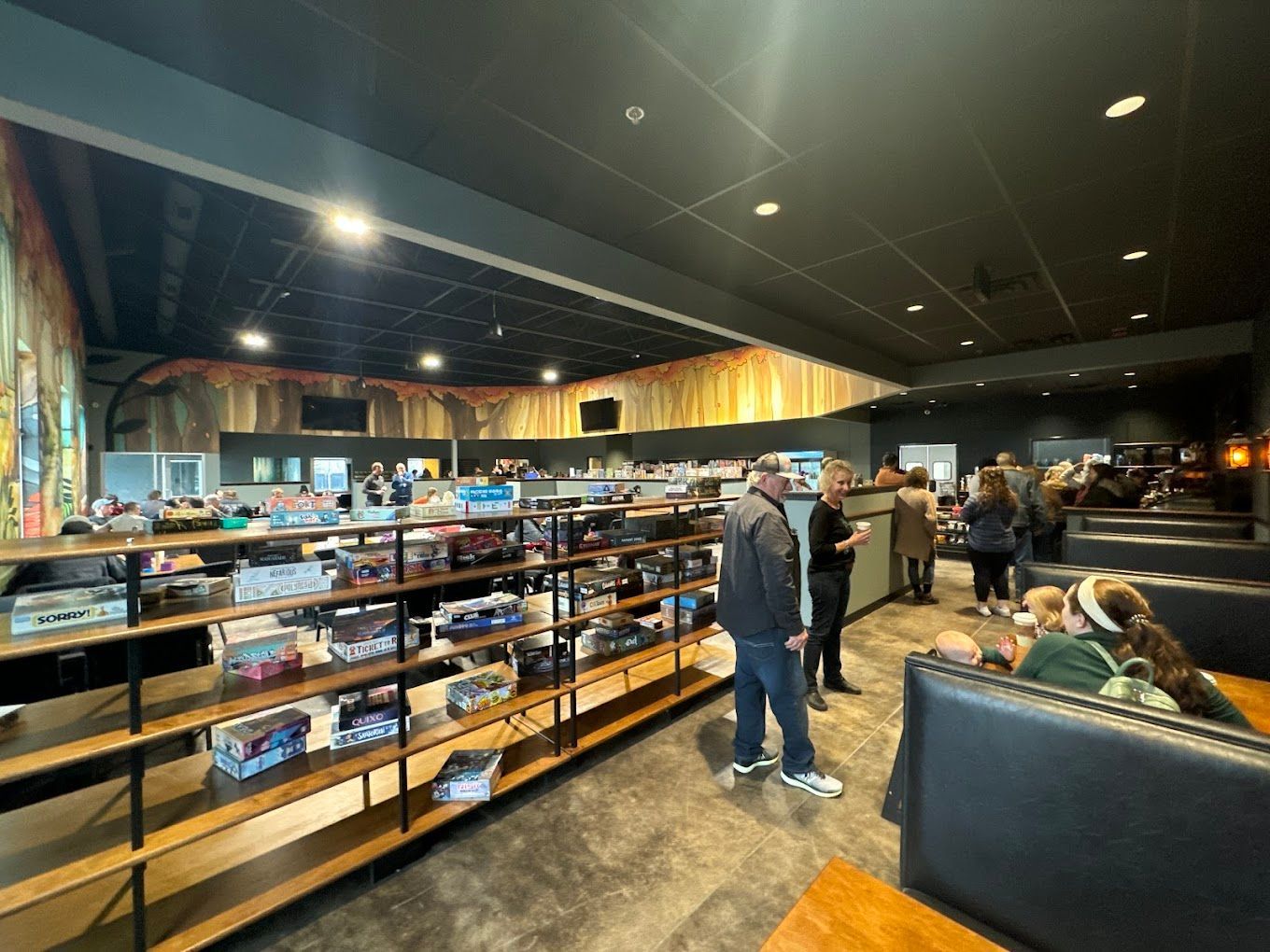 Interior of a board game store, with shelves of games, customers browsing, and seating.