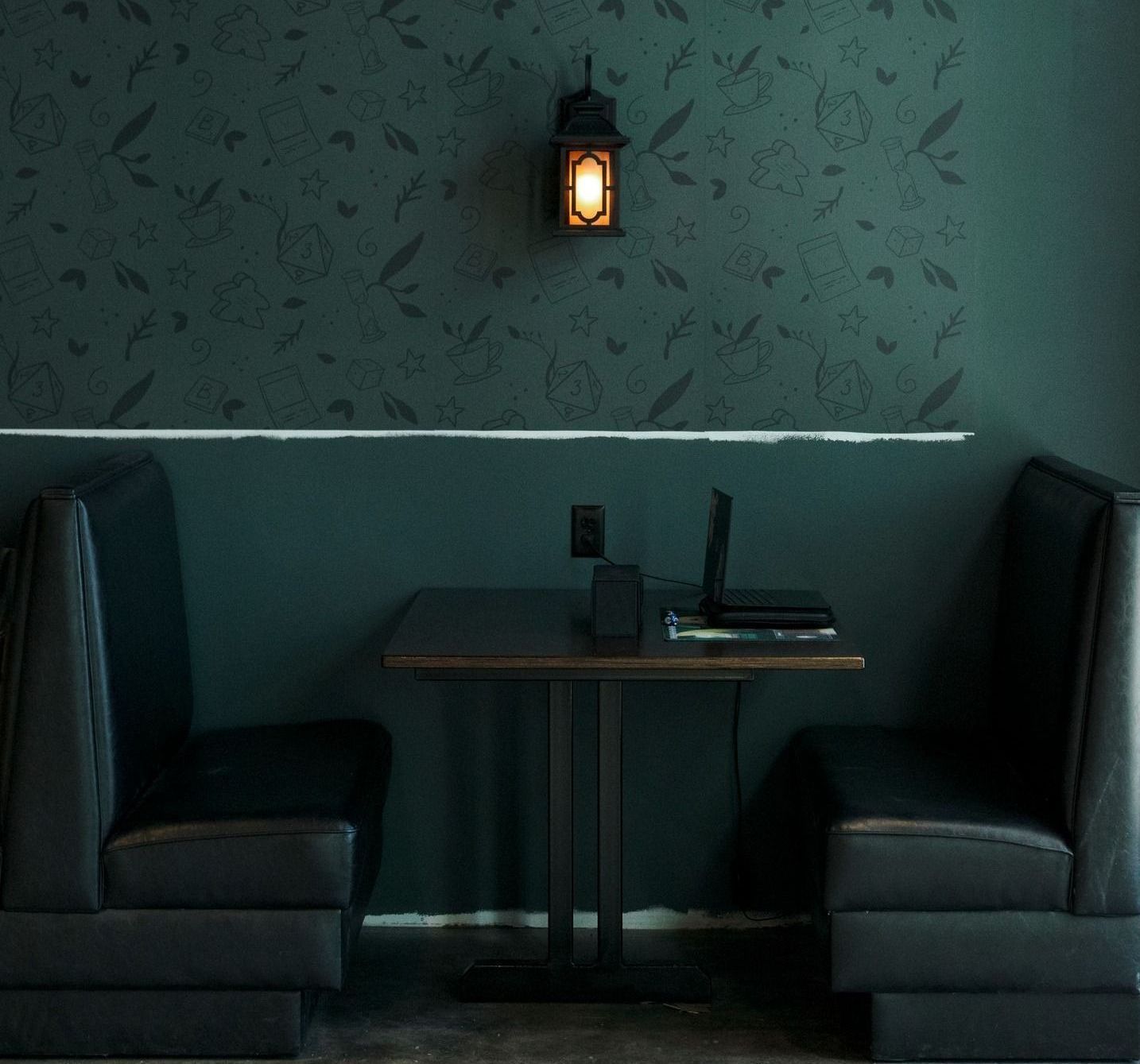 Dark booth seating with a small table, laptop, and wall-mounted lantern against a dark green textured wall.