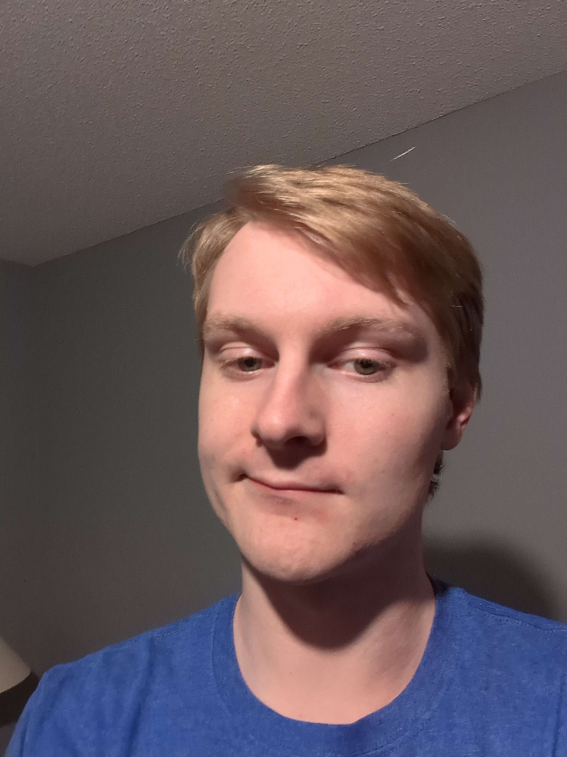 Young person with light hair and blue shirt smirking, looking towards the camera.