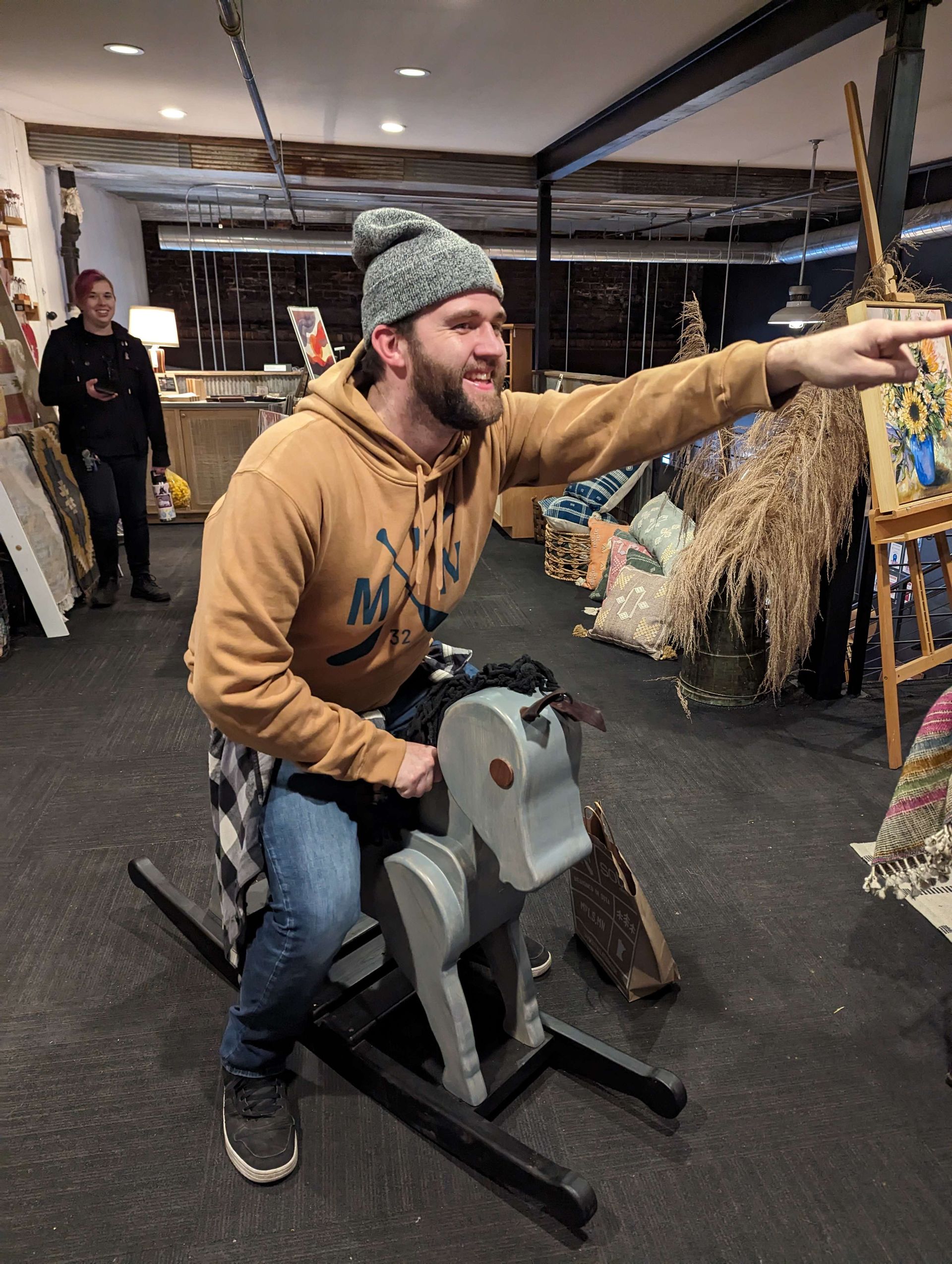 Man on rocking horse, pointing with excited expression in shop setting.