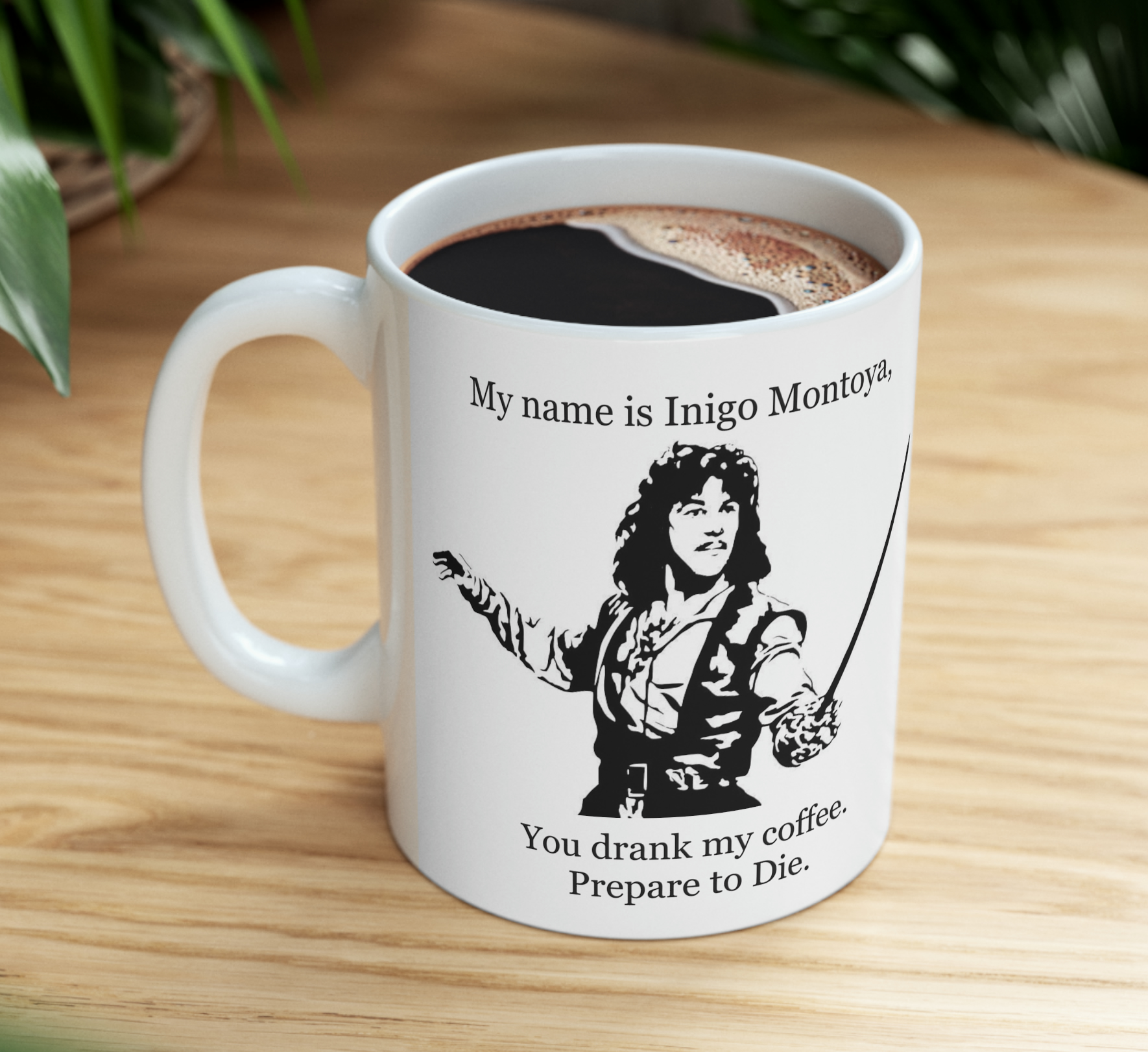 White mug on wooden table with “My name is Inigo Montoya” and a black swordfighter graphic.