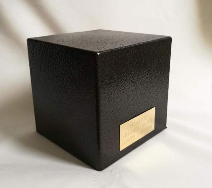 Cubo de color marrón oscuro con superficie texturizada, pequeña placa dorada en el frente.