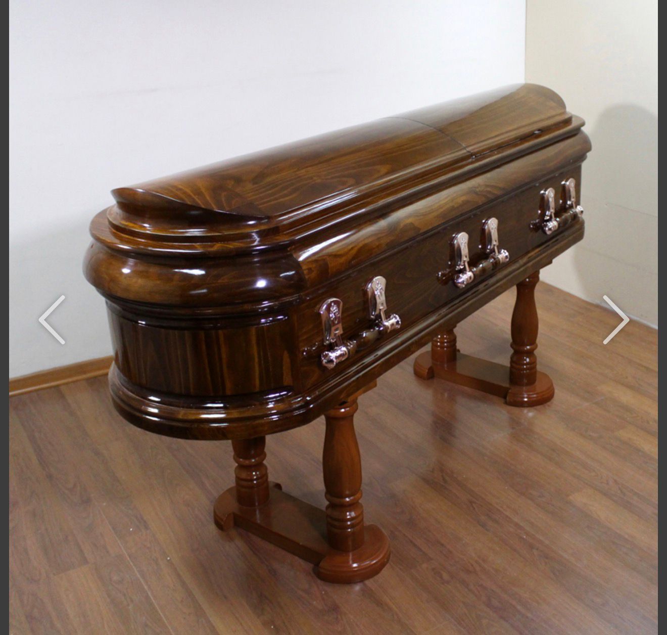 Ataúd de madera sobre un soporte de madera en una habitación, con un acabado oscuro y brillante.