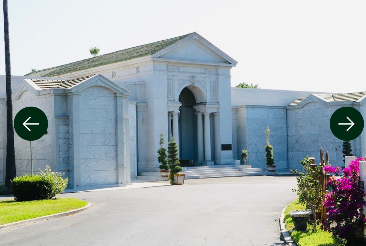 Cementerio verde y exuberante con dosel de árboles, luz solar sobre las lápidas y flores esparcidas.