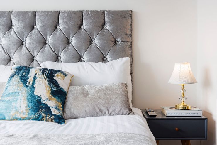Gray tufted headboard with white bedding, patterned pillows, and a bedside lamp on a nightstand