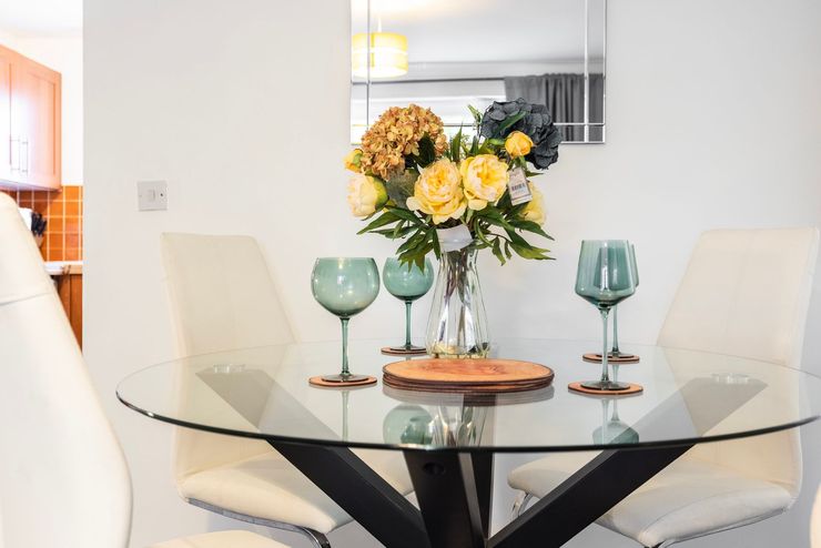 Glass dining table with flowers, two wine glasses, and beige chairs in a bright room