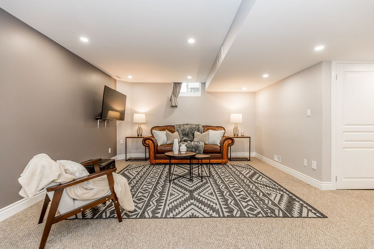 Basement with a brown leather sofa, rug, and TV on the wall.