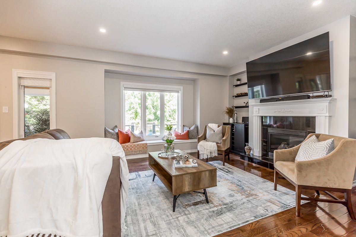 Living room with fireplace, window seat, and large TV; neutral tones and wood flooring.