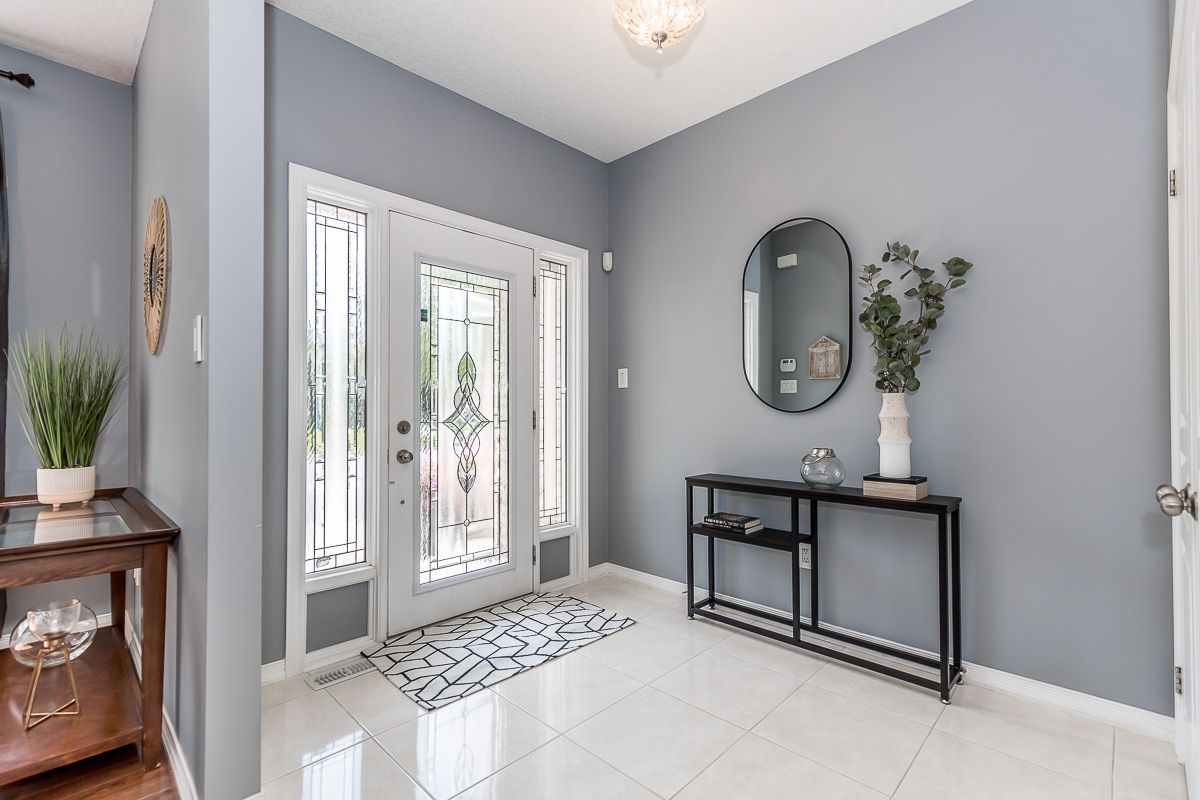 Entryway with gray walls, white tile floor, front door, console table, mirror, and greenery.
