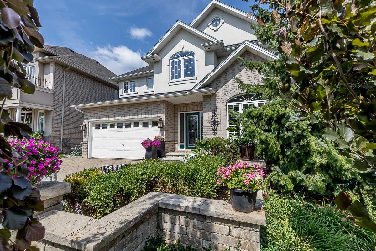 Two-story house, arched windows, and white garage door. Landscaping with flowers and greenery.
