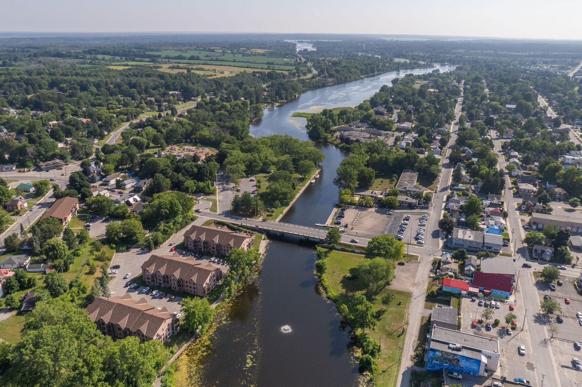 Aerial view of a river running through a town with trees, buildings, and a bridge.