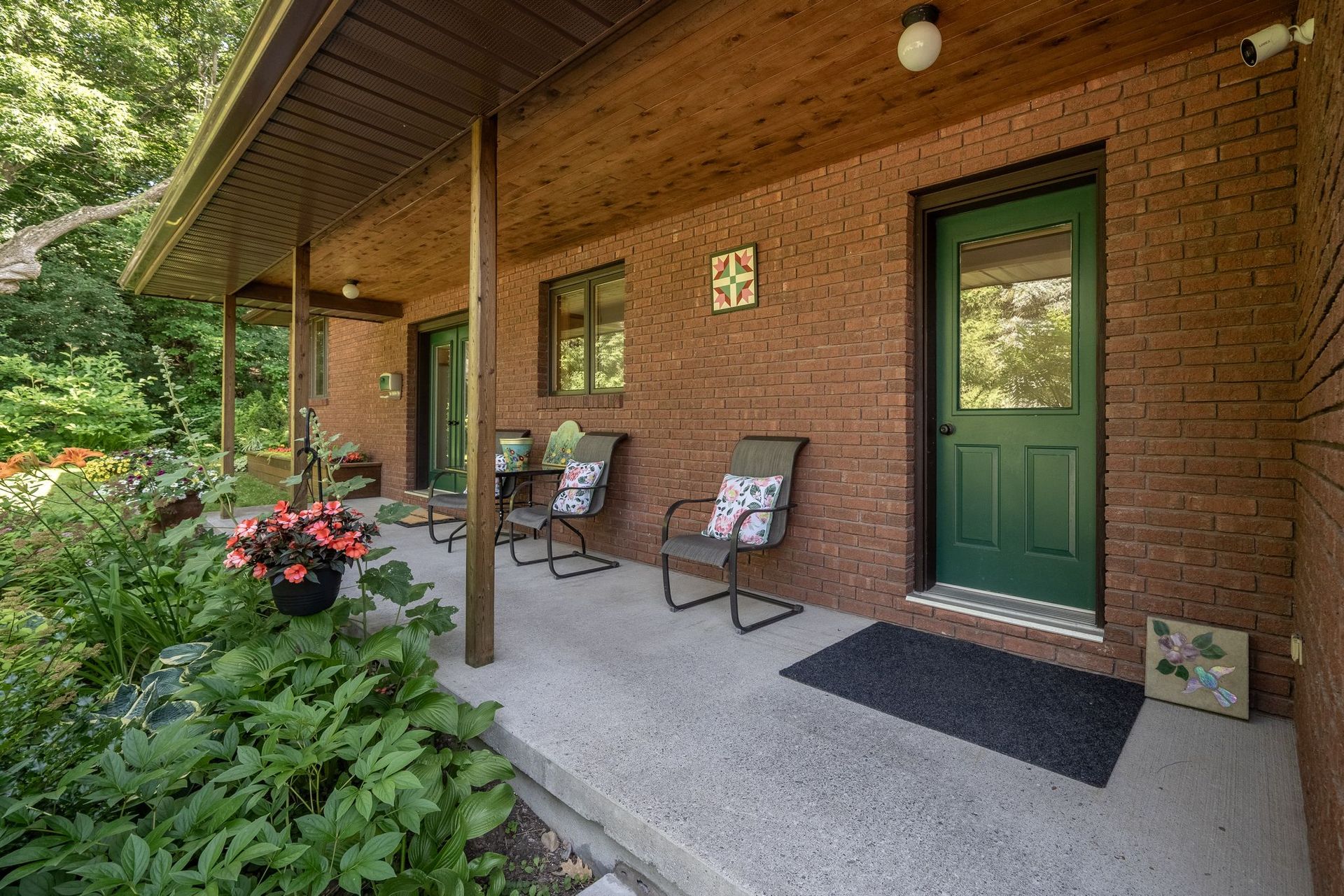 Brick house exterior with porch, green door, and seating. Lush garden to the side.