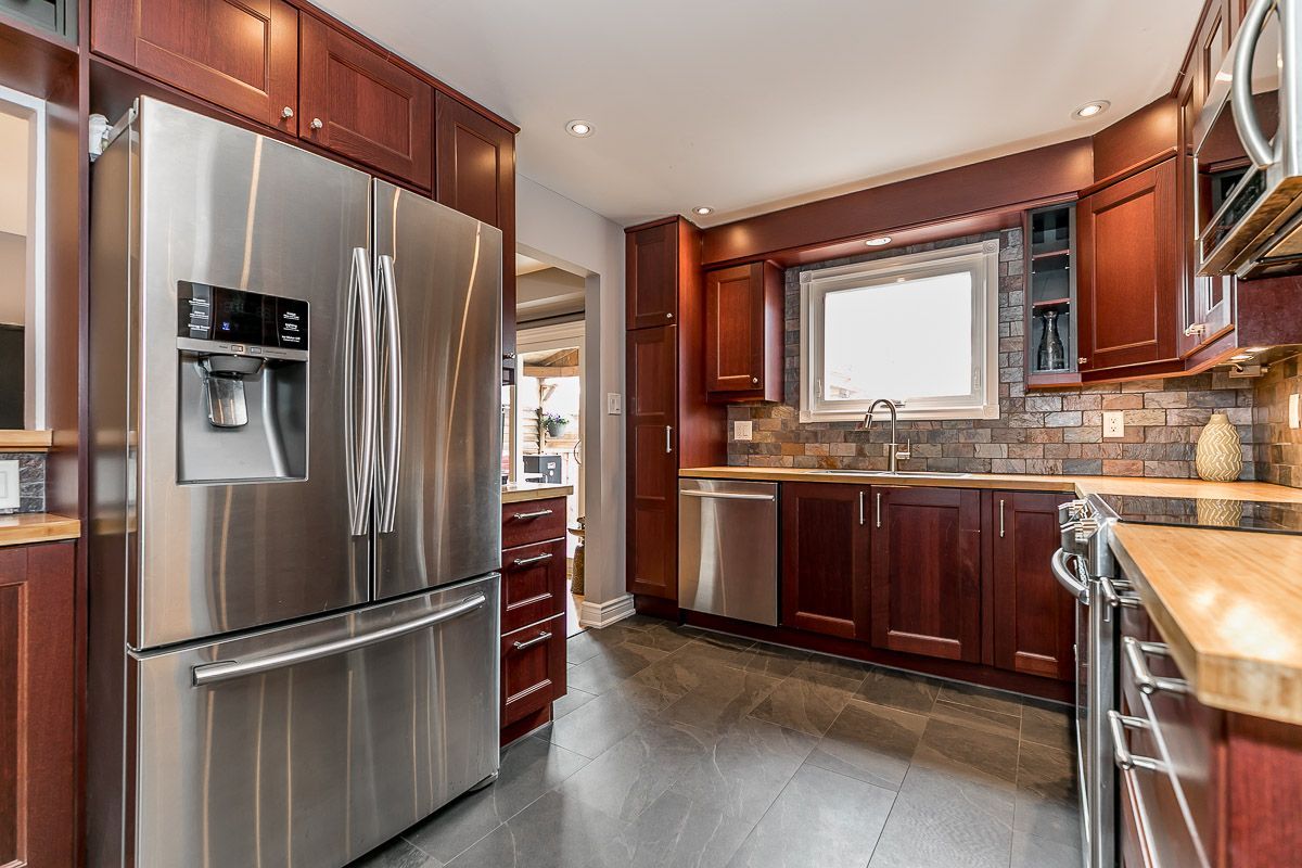 Stainless steel refrigerator in a kitchen with dark wood cabinets and gray flooring.