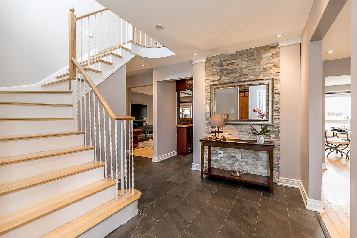 Foyer with staircase and stone accent wall, mirror, table, and dark gray tile floor.