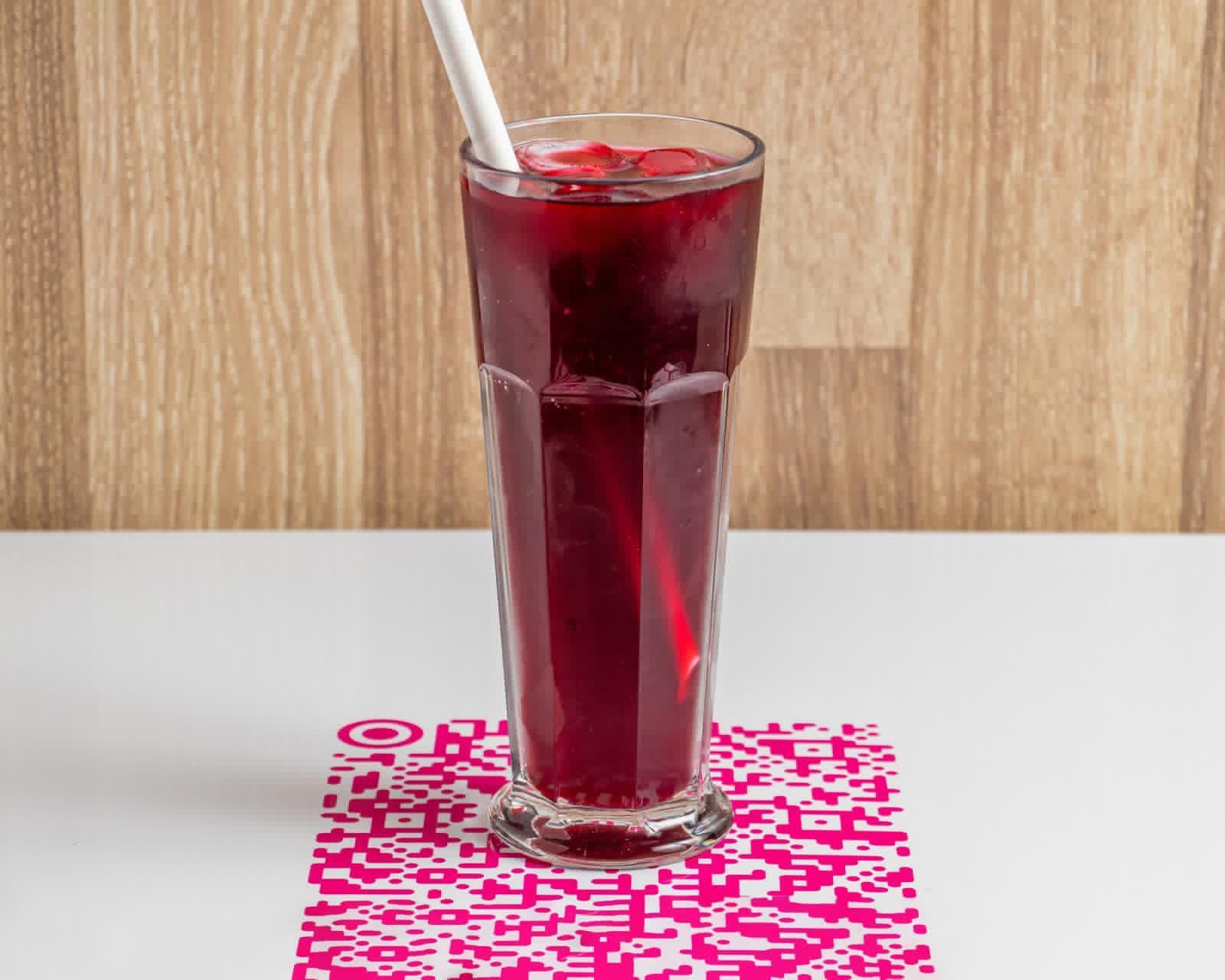 Smoothie aux baies dans une tasse transparente sur une surface noire, avec des glaçons et un gaufrier en arrière-plan.