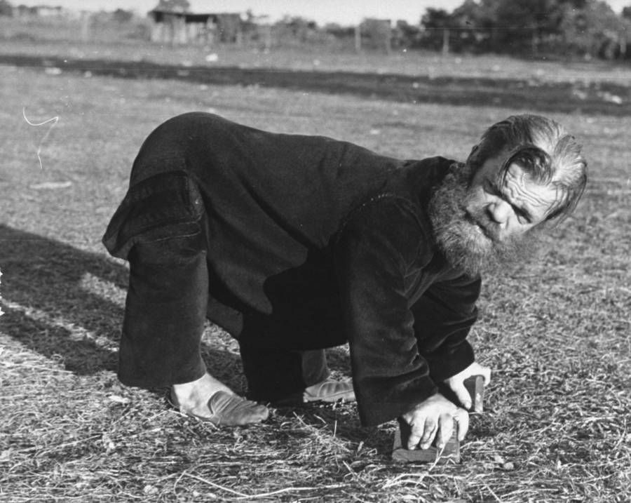 A man in dark clothing, hunched over on hands and feet, on a grassy field.
