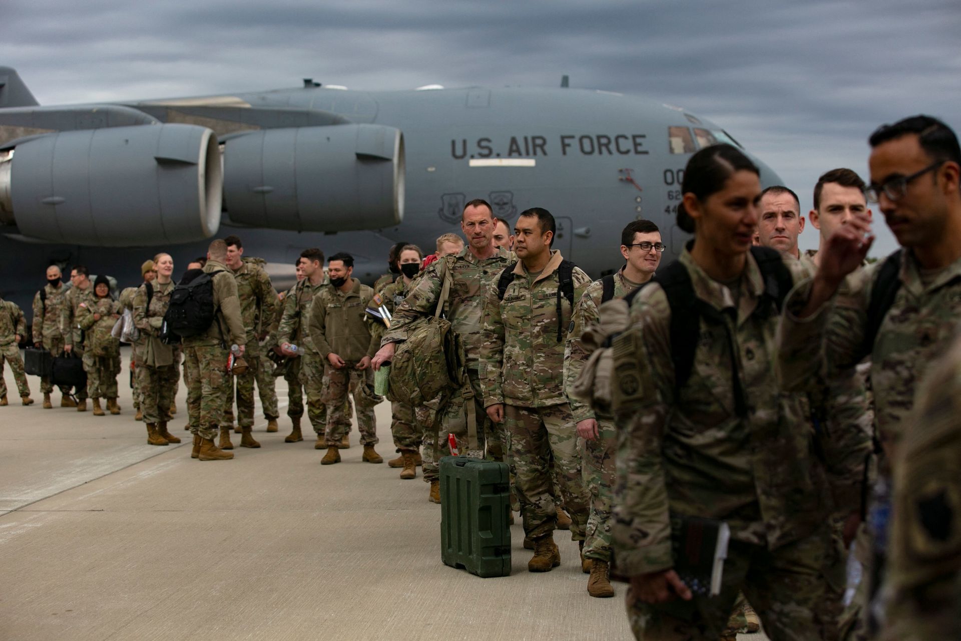 U.S. Air Force personnel in camouflage uniforms disembarking a C-17 cargo plane on a tarmac.