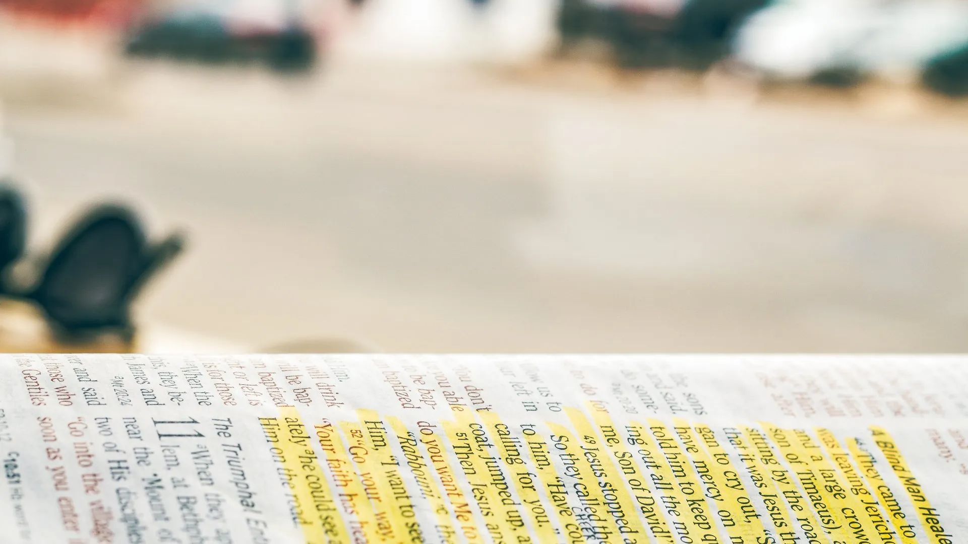 Open Bible with highlighted text, blurry background of a street scene.