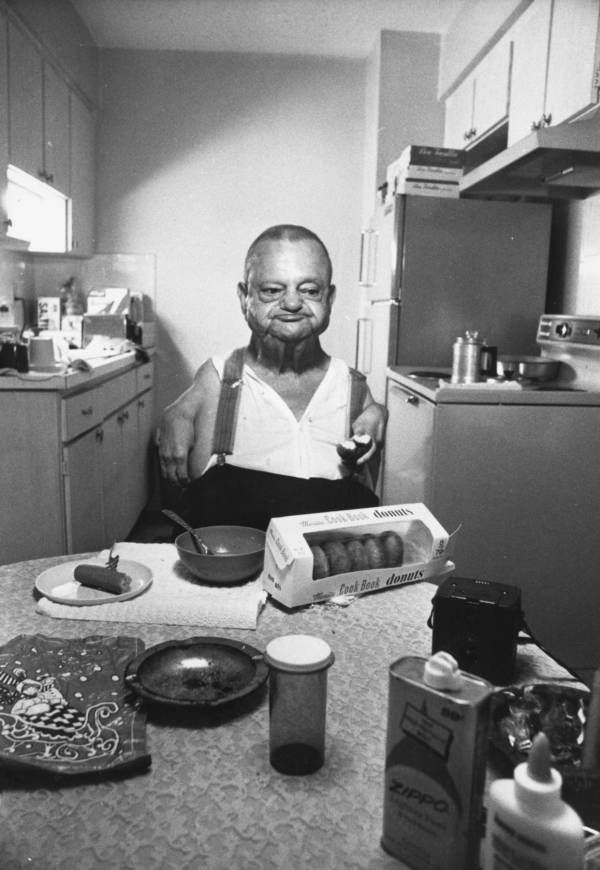 Man seated at a kitchen table; breakfast of eggs and toast in front of him.