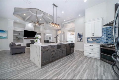 Modern open-concept kitchen with gray island, white cabinets, blue tile backsplash, and vaulted ceiling