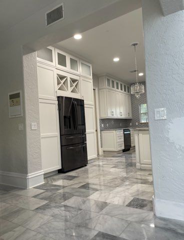 Modern kitchen with black refrigerator, white cabinets, and gray marble tile flooring viewed from an entryway