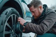 Man in jacket cleans a car tire's rim with a brush, outdoors.