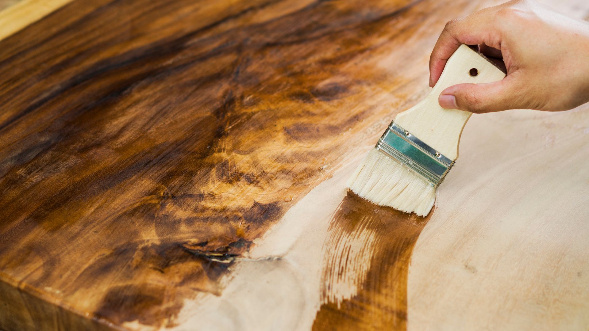 Applicazione manuale di una leggera finitura su una superficie in legno con un pennello.