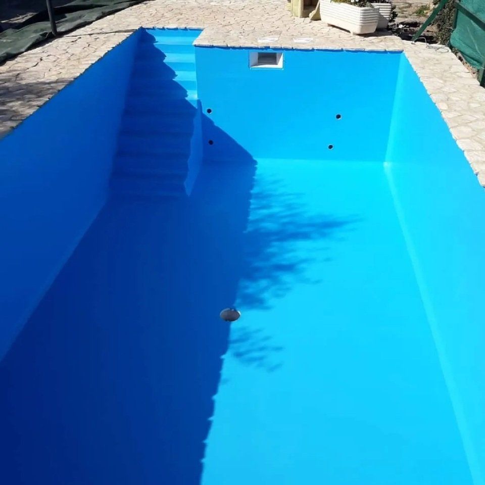 Piscina vuota di un azzurro brillante con scalini sulla sinistra e pavimentazione in pietra tutt'intorno.