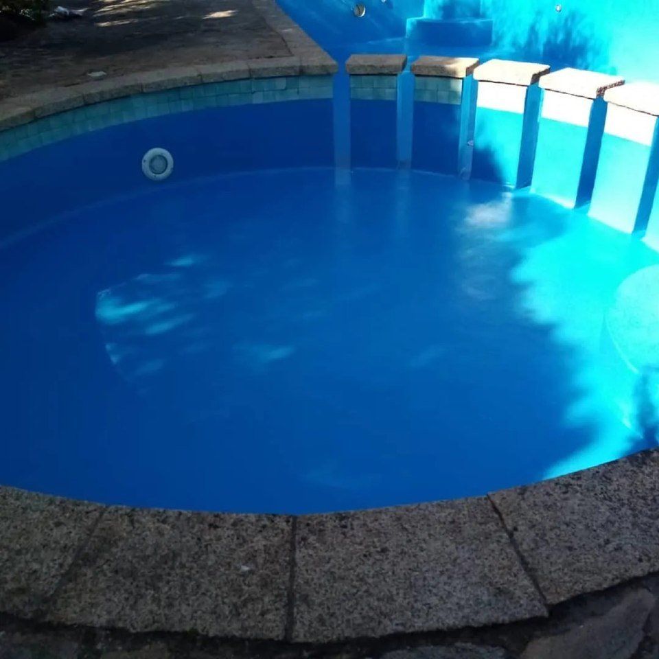 Piscina vuota di colore blu con bordo in pietra e riflessi di luce solare.