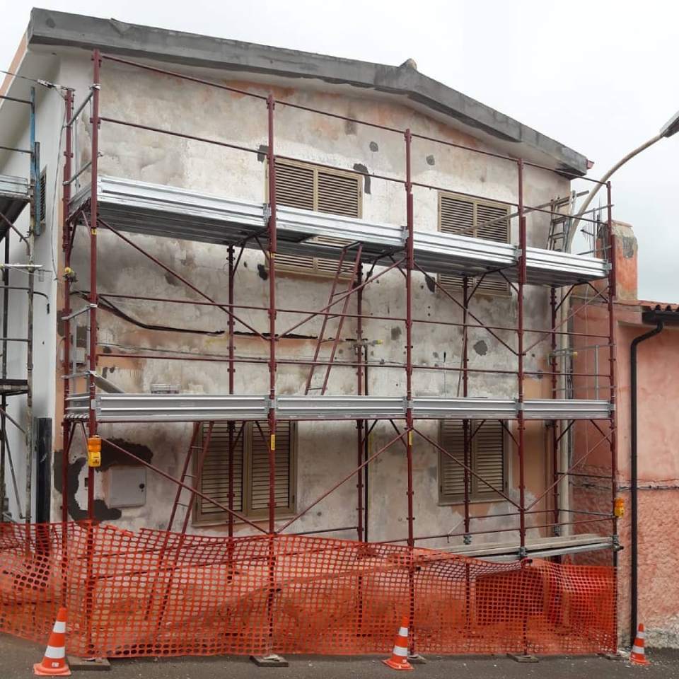 Ponteggi e reti di sicurezza arancioni attorno alla facciata di un edificio in fase di ristrutturazione.