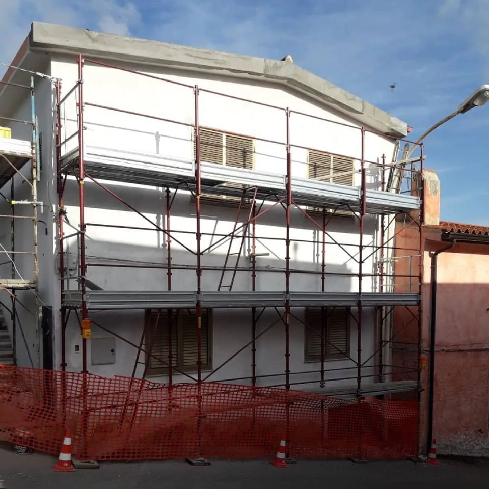 Casa bianca in costruzione con impalcature metalliche e recinzioni di sicurezza arancioni.