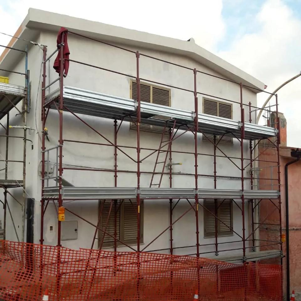 Edificio in fase di ristrutturazione con impalcature metalliche e reti di sicurezza arancioni lungo la facciata.