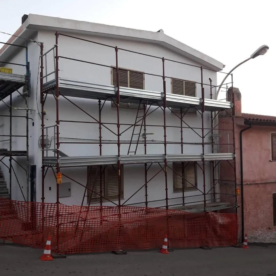 Casa bianca a due piani sotto impalcature e rete di sicurezza arancione all'angolo di una strada