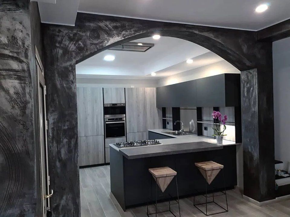 Cucina moderna in bianco e nero e grigio con apertura ad arco, isola e due sgabelli da bar.